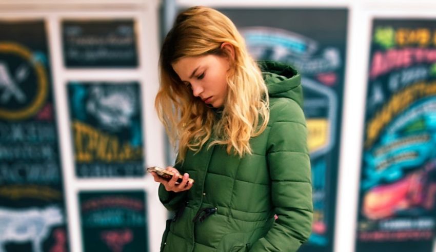 A woman in a green jacket is looking at her phone.