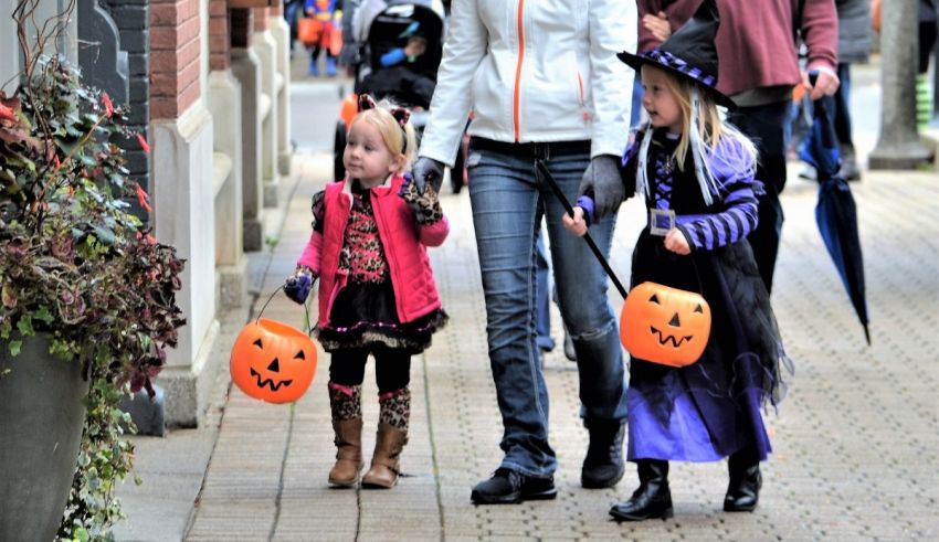 A woman and two children dressed in halloween costumes walking down a sidewalk.