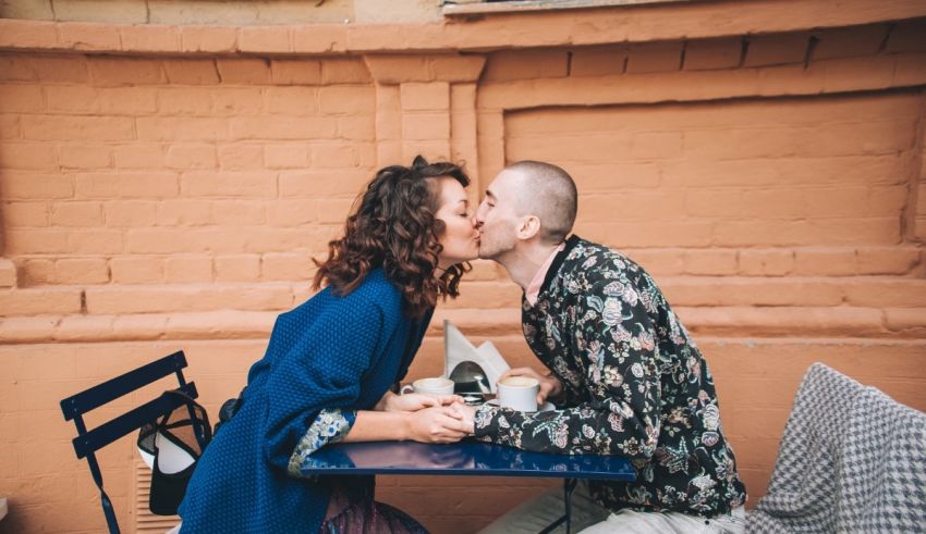 A couple kissing at a table in front of a brick wall.