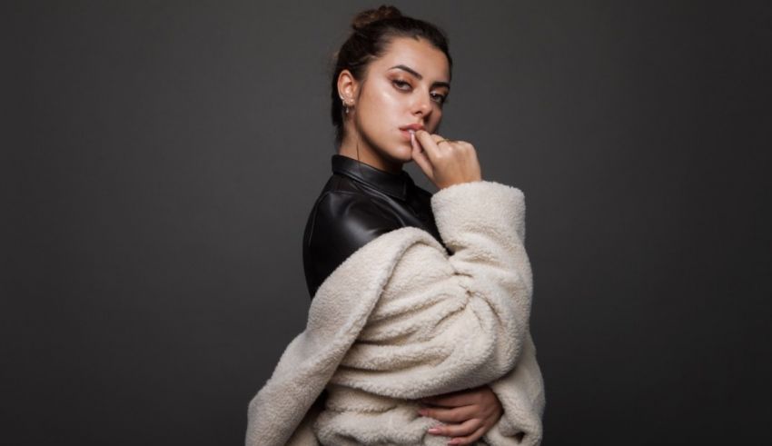 A young woman in a white fur coat posing on a grey background.