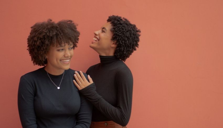 Two black women laughing against an orange wall.