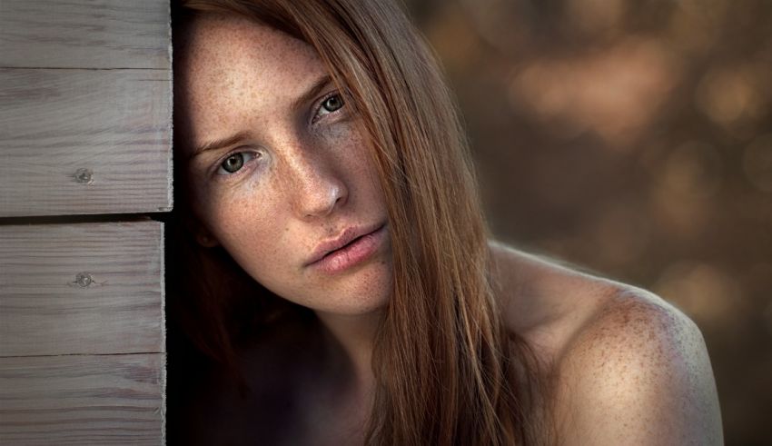 A woman with freckles leaning against a wooden wall.