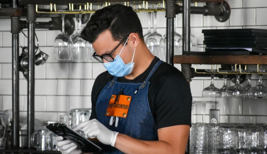 A bartender wearing a face mask and glasses working in a restaurant.
