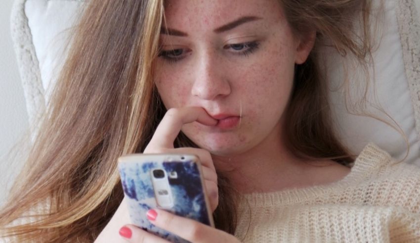 A young woman looking at her phone while laying in bed.