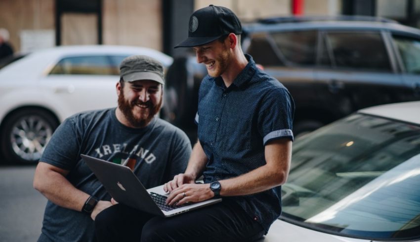 A man sitting on a car with a laptop.