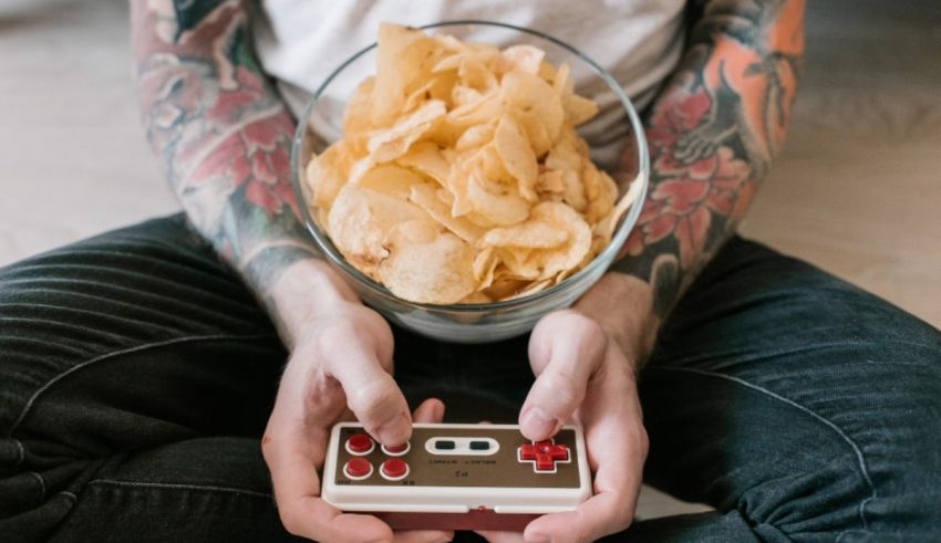 A man with tattoos holding a nintendo controller and chips.