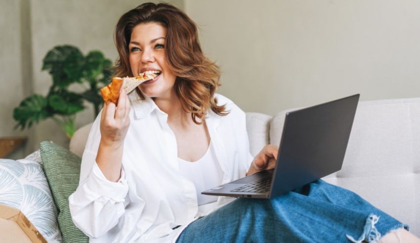 A woman eating pizza while sitting on a couch with a laptop.