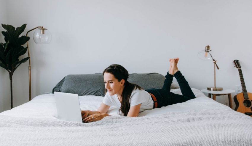 A young woman laying on a bed using her laptop.