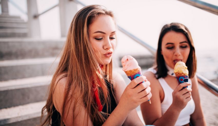 Two young women eating ice cream cones at the beach.