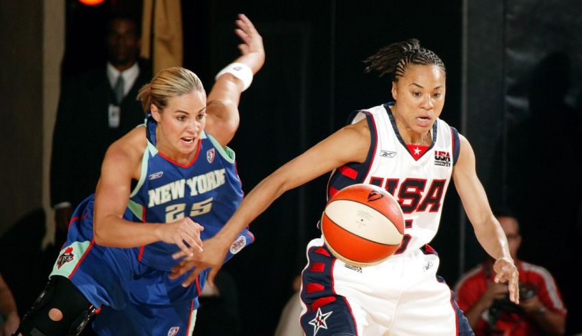 Two women playing basketball in front of a crowd.