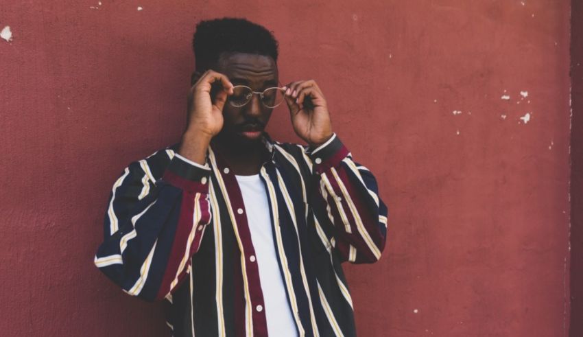 A black man in a striped shirt leaning against a wall.