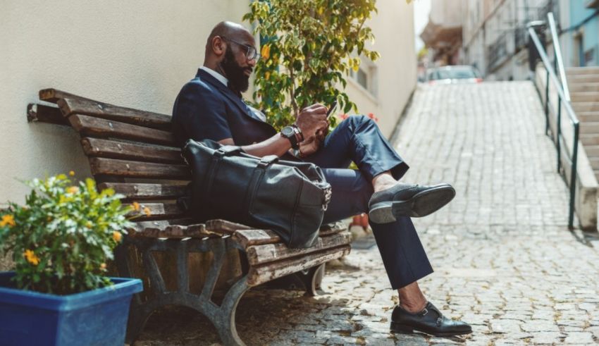 A man in a suit sitting on a bench and using his phone.
