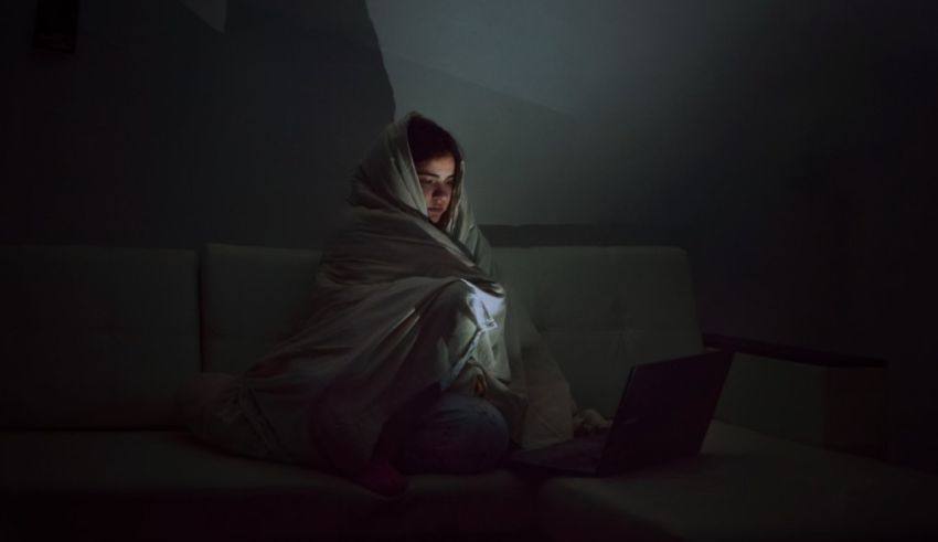 A woman wrapped in a blanket sitting on a couch with a laptop.
