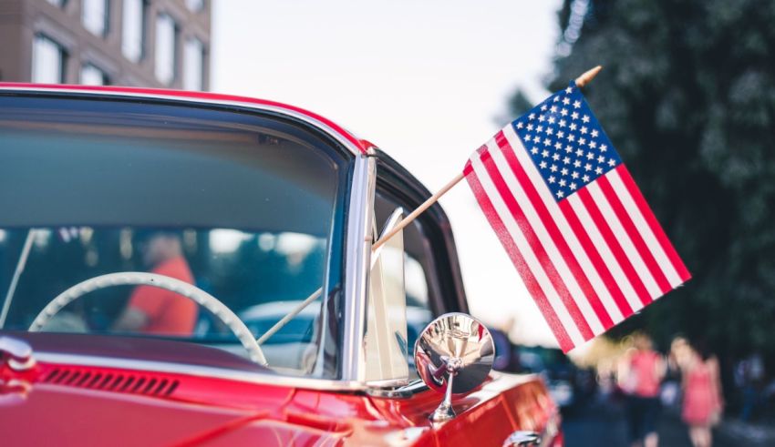 An american flag hangs from the rear window of a classic car.