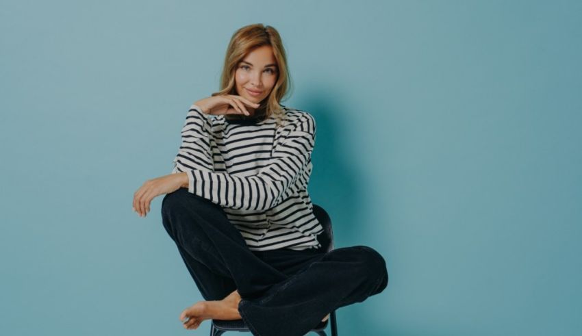 A young woman in a striped sweater sitting on a chair against a blue background.