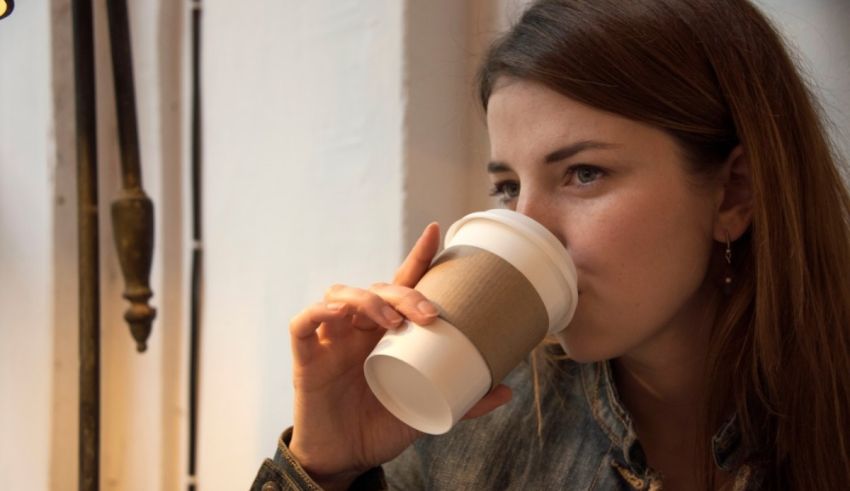 A woman drinking coffee from a paper cup.