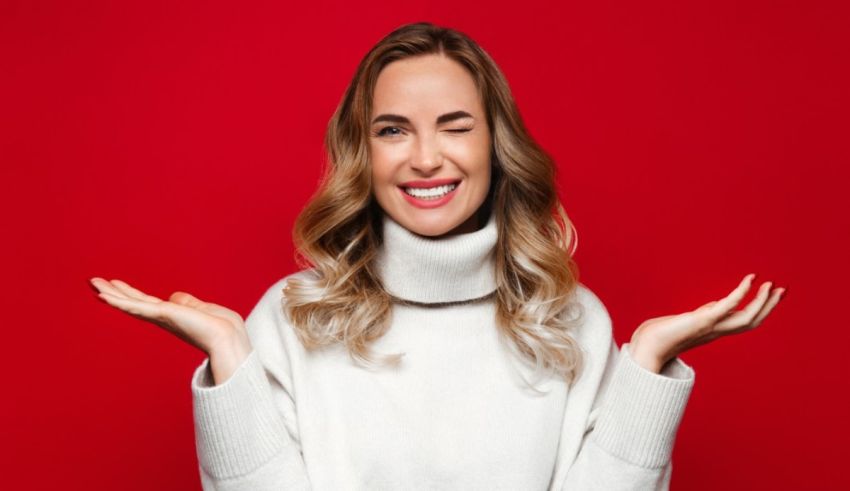 A young woman in a white sweater with her hands outstretched on a red background.