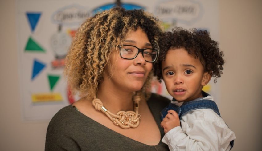 A woman with glasses holding a child in front of a wall.