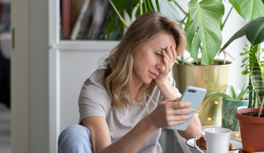 A woman looking at her phone while sitting in front of a plant.