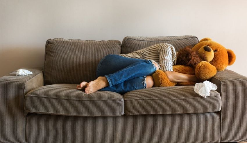 A woman sleeping on a couch with a teddy bear.