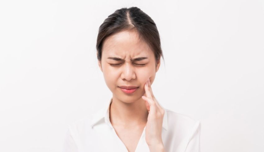 A young asian woman with a toothache on a white background.