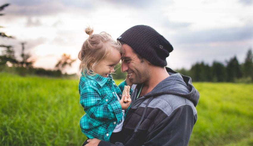 A man and his daughter in a field at sunset.
