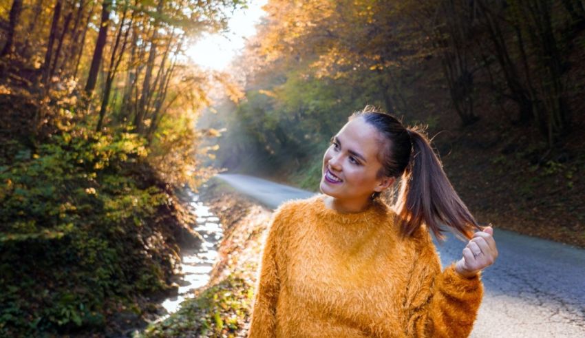 A young woman in an orange sweater is standing on a road in the forest.