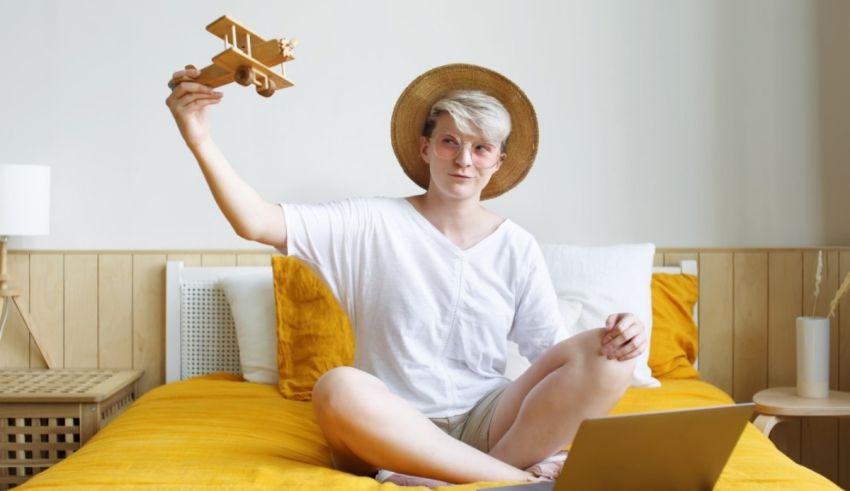 A young man sitting on a bed with a laptop and a toy airplane.