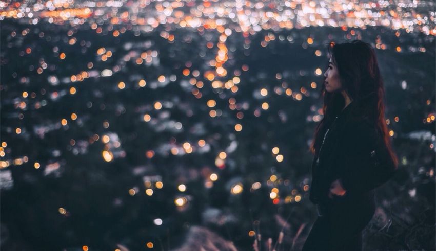 A woman standing on a hill overlooking a city at night.