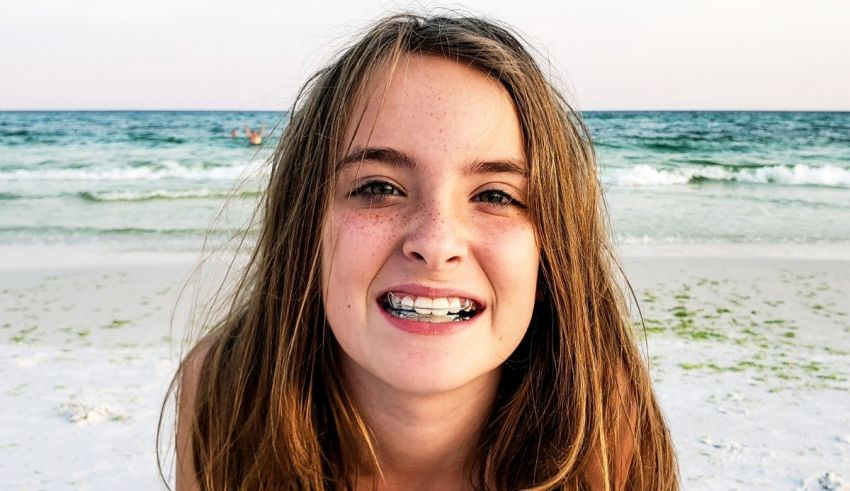 A young girl smiling on the beach with braces.