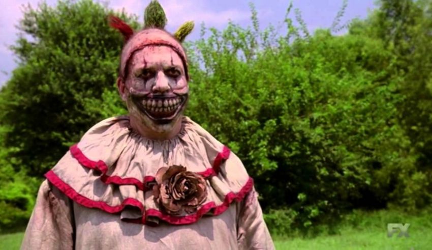 A clown dressed in a costume is standing in a field.