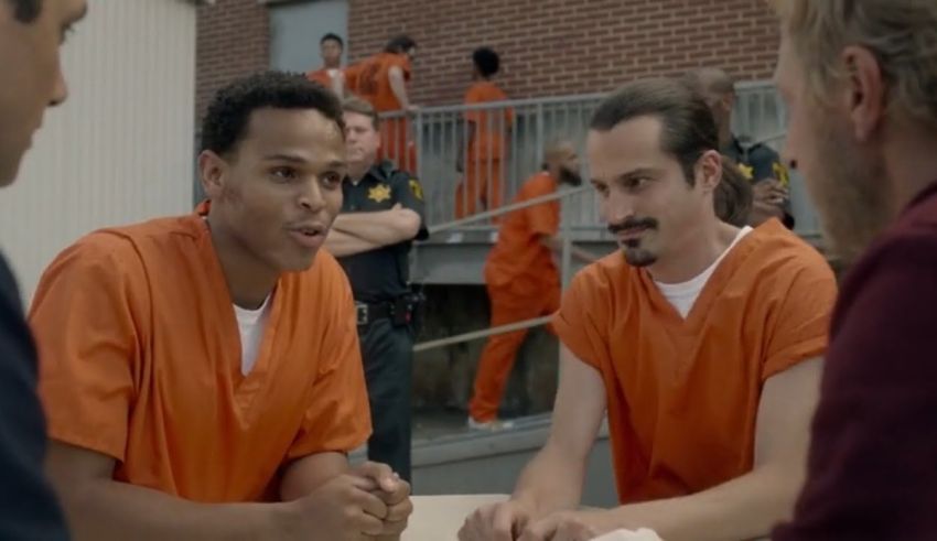 A group of men sitting around a table in an orange prison uniform.