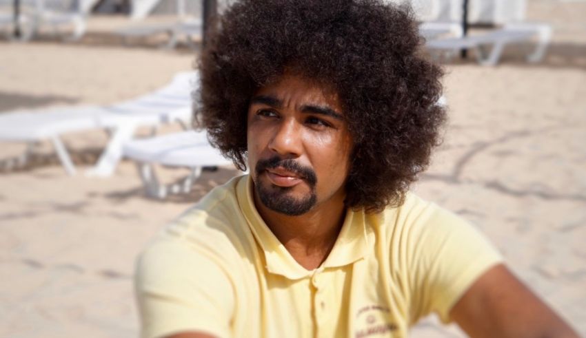 A man with afro hair sitting on the beach.