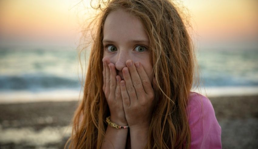 A girl covering her mouth with her hands on the beach.