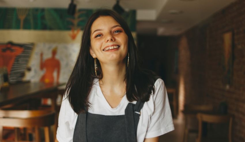 A smiling woman in an apron standing in a restaurant.
