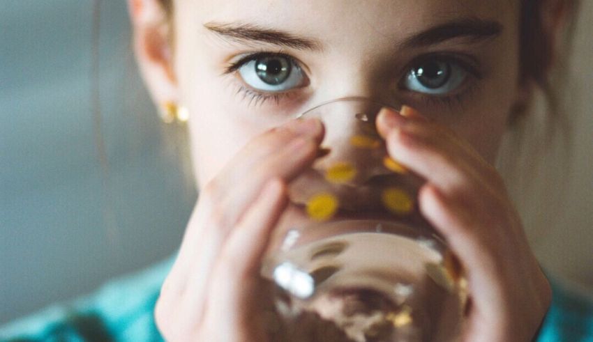 A young girl drinking water from a glass.