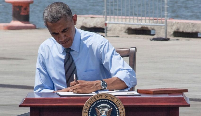 President barack obama signs a document in front of a body of water.