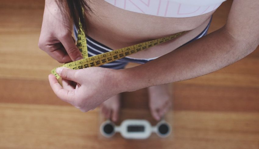 A woman is measuring her waist with a measuring tape.