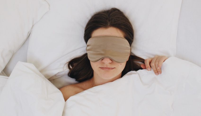 A woman laying in bed with a beige eye mask.