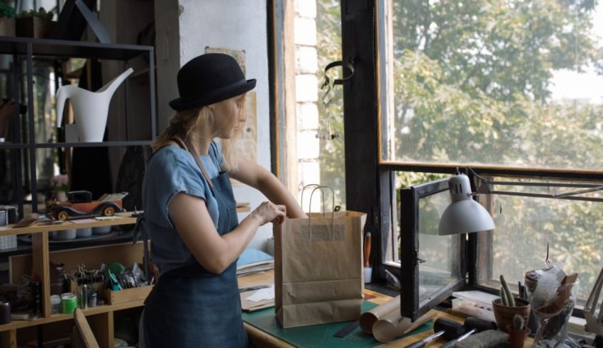 A woman in an apron is holding a paper bag in front of a window.