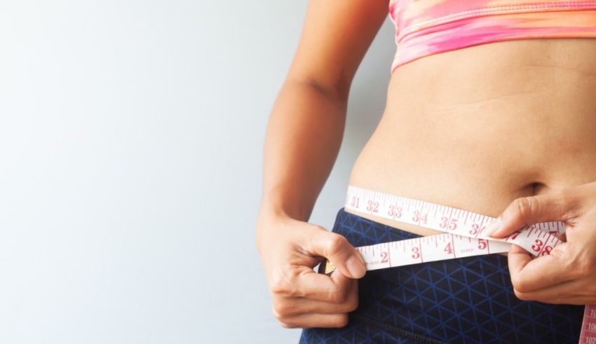 A woman is measuring her waist with a measuring tape.