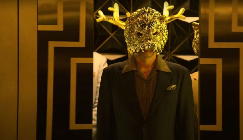 A man in a suit with a gold mask standing in an elevator.