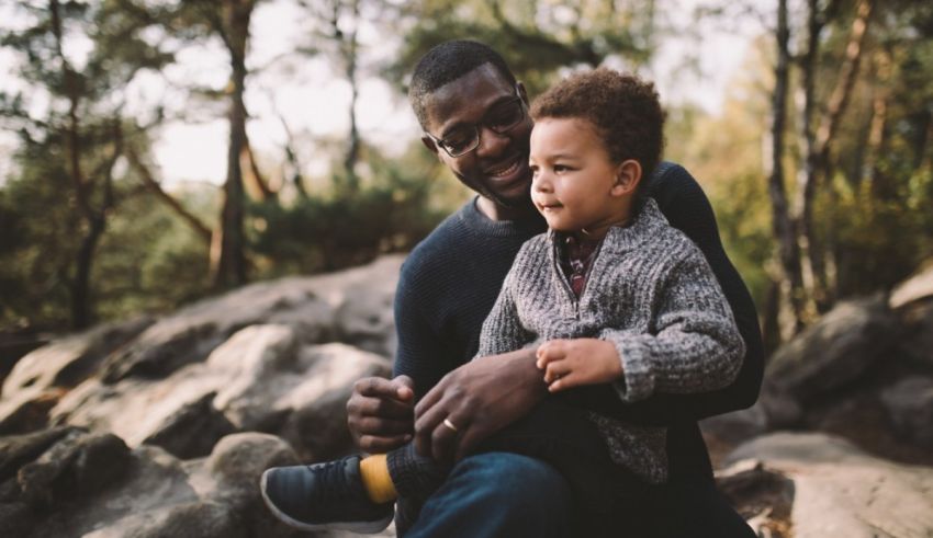 An african-american father holding his son in the woods.