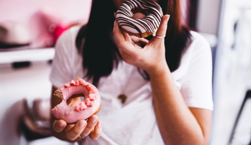 A woman is eating two donuts in a bakery.