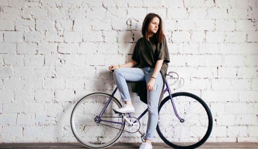 A young woman leaning against a white brick wall with a purple bicycle.