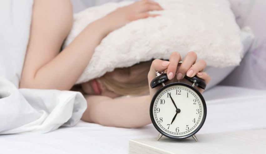 A woman sleeping in bed with an alarm clock.