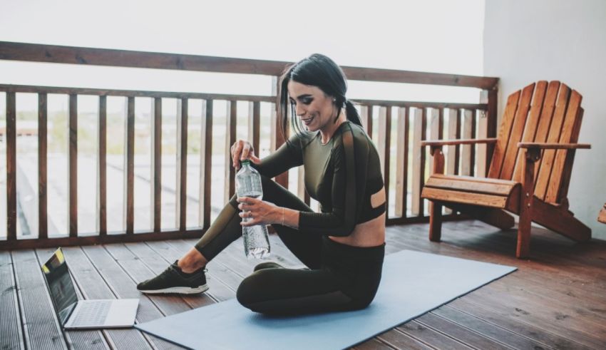 A woman sitting on a yoga mat with a laptop on her lap.