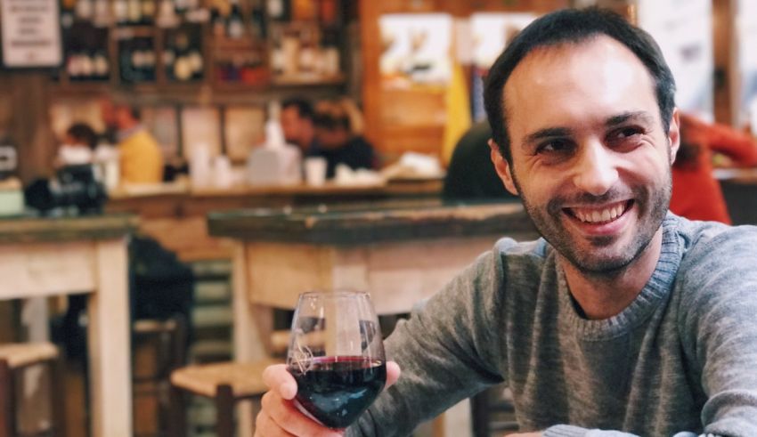 A man smiles while holding a glass of red wine.