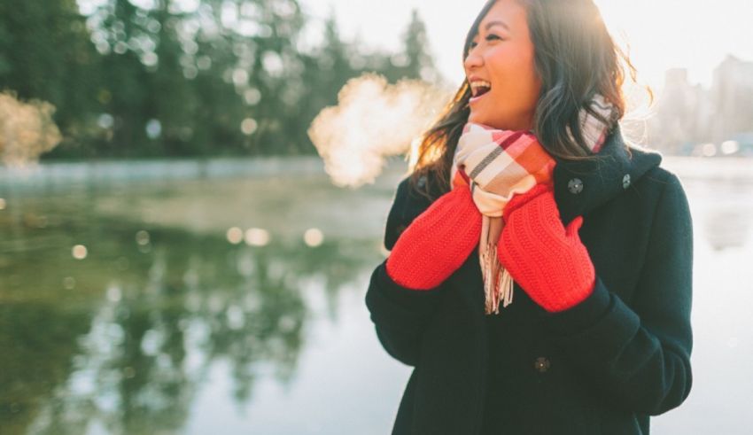 A woman in a red coat and red gloves standing near a lake.