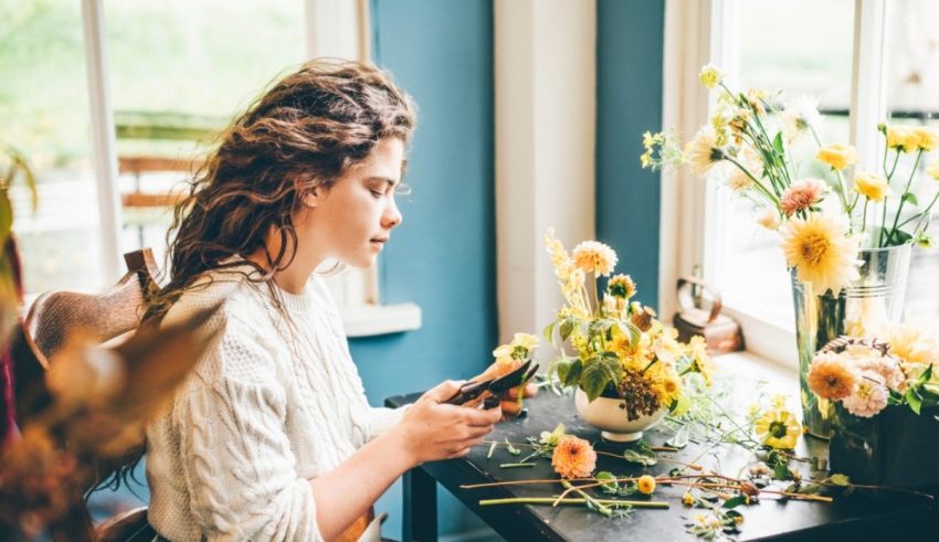 A woman is using her phone while sitting at a table with flowers.